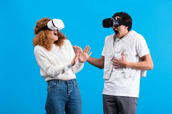 beautiful excited couple using virtual reality headsets, isolated on blue