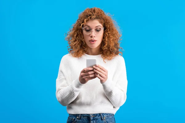 Surprised Redhead Woman Eyeglasses Using Smartphone Isolated Blue — 스톡 사진