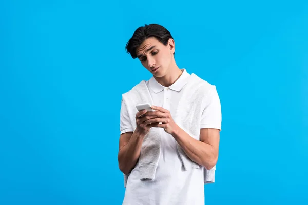 Skeptical Young Man Using Smartphone Isolated Blue — Stock Photo, Image