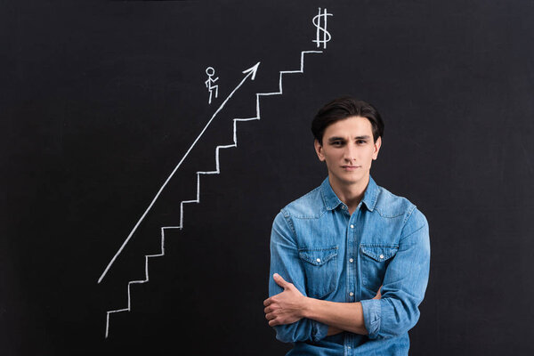 confident young man with crossed arms and blackboard with startup and business growth drawing 