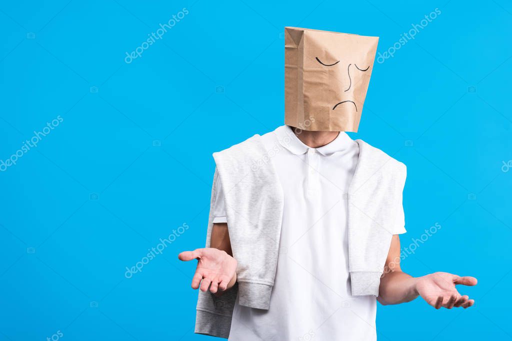 skeptical man with sad paper bag on head, isolated on blue