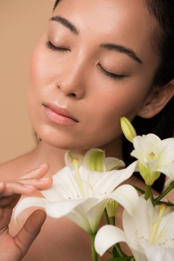beautiful naked asian girl with closed eyes and white lilies isolated on beige clipart