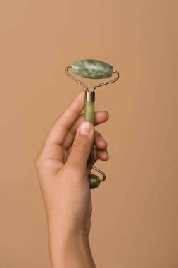 cropped view of woman holding jade roller isolated on beige clipart