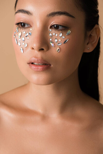 beautiful naked asian girl with rhinestones on face isolated on beige