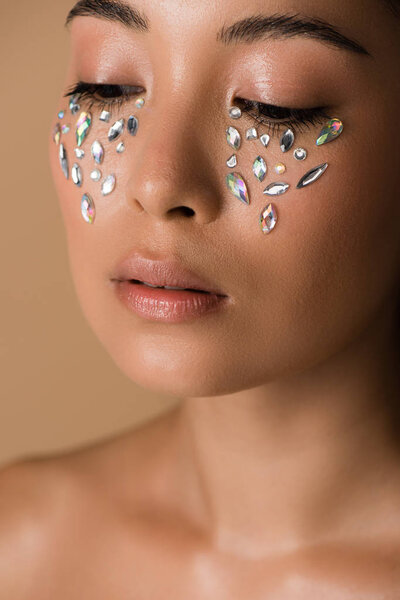 close up view of beautiful naked asian girl with rhinestones on face isolated on beige
