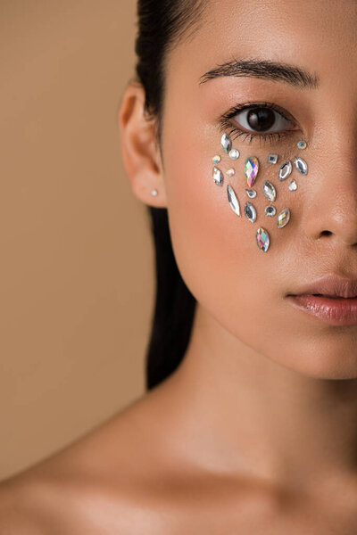 cropped view of beautiful naked asian girl with rhinestones on face isolated on beige