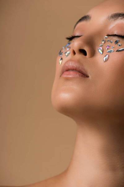 beautiful asian girl with rhinestones on face and closed eyes isolated on beige