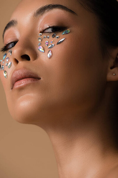 low angle view of beautiful asian girl with rhinestones on face isolated on beige