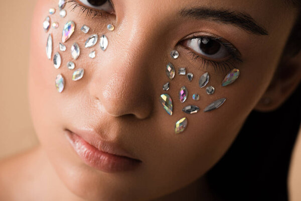 close up view of beautiful naked asian girl with rhinestones on face isolated on beige