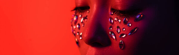 cropped view of beautiful naked asian girl with rhinestones on face isolated on red, panoramic shot