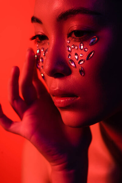 beautiful naked asian girl touching face with rhinestones isolated on red