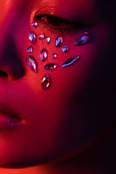 close up view of beautiful asian girl with rhinestones on face in red light