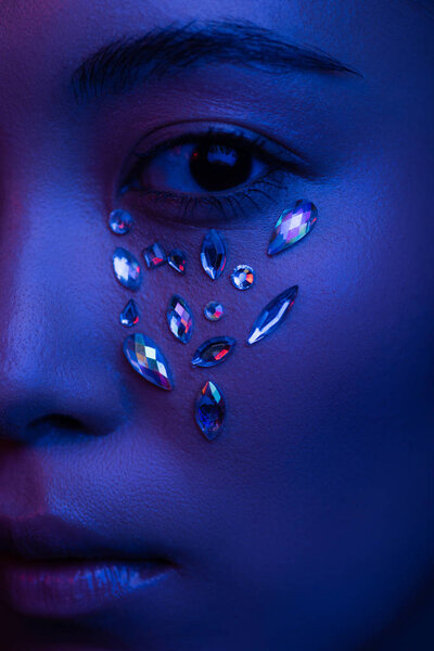 close up view of beautiful asian girl with rhinestones on face in blue light
