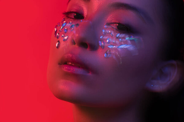 beautiful asian girl with rhinestones on face isolated on red, motion blur