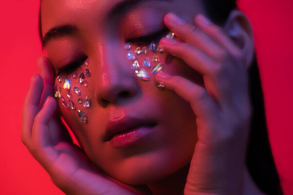 beautiful asian girl touching face with rhinestones isolated on red, motion blur