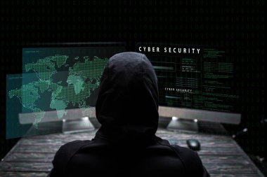 back view of hooded hacker sitting near computer monitors with cyber security lettering on black  clipart