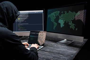 Bilgisayar ekranında siber güvenlik harfleri olan bir bilgisayar korsanı siyah ekranda bilgisayar monitörleri kullanıyor. 