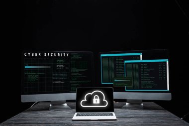 Bilgisayar monitörlerinin yanında bulut ve asma kilit olan bilgisayar ve siber güvenlik harfleri siyah üzerine izole edilmiş. 