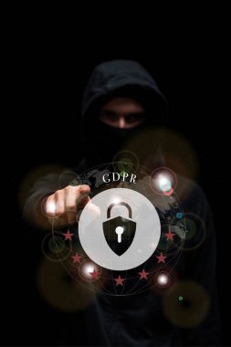 selective focus of hacker in hood pointing with finger at gdpr lettering on black  clipart