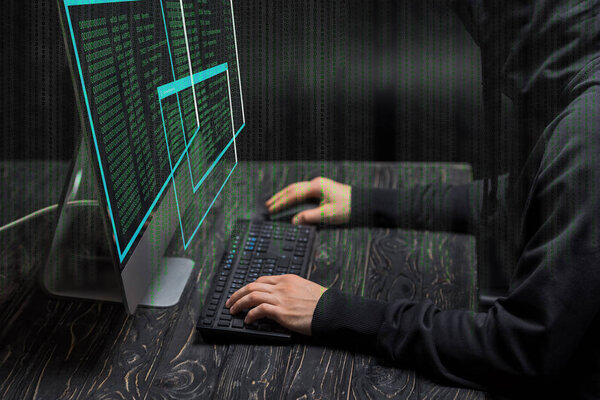 cropped view of hacker typing on computer keyboard near computer monitor with data on black 