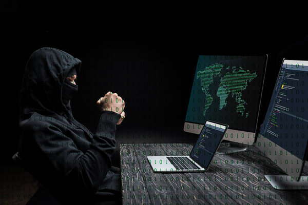 hacker with clenched fists looking at laptop with near computer monitors with world map on black 