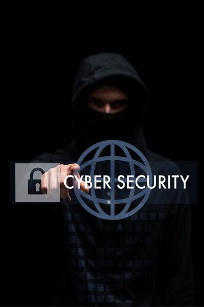 selective focus of hacker in hood pointing with finger at cyber security lettering on black 