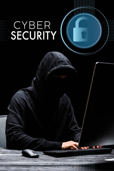 hacker sitting near computer monitor and typing on computer keyboard near cyber security lettering on black 
