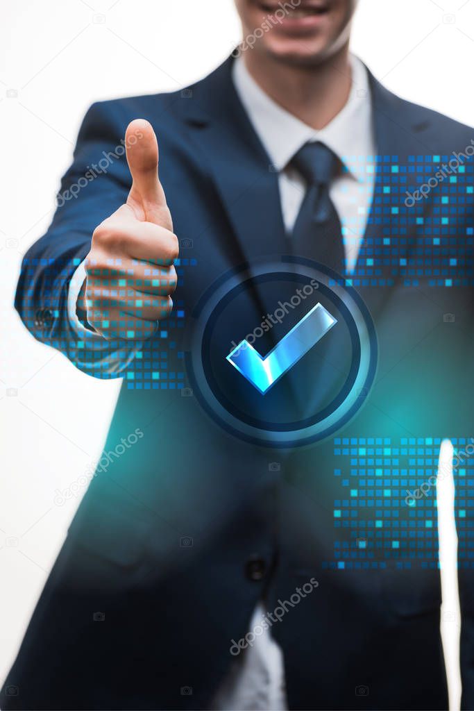 selective focus of happy businessman in suit showing thumb up near check mark on white 