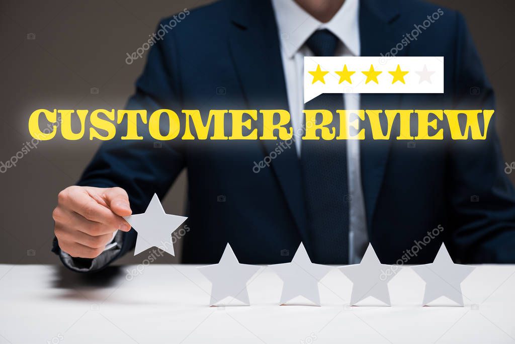 cropped view of businessman holding star near customer review lettering on grey, quality concept 