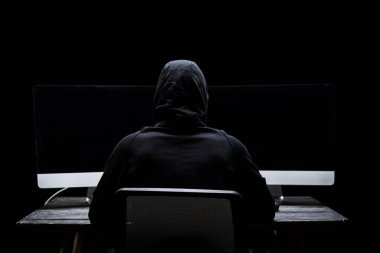 Siyah ekranda boş ekranı olan bilgisayar monitörlerinin yanında oturan hacker 'ın arka görünümü 