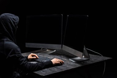Bilgisayar faresi kullanan bilgisayar korsanı ve boş ekranlı bilgisayar monitörlerine siyah ekranda bakıyor 