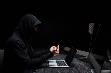 Bilgisayarın yanında orta parmağı ve siyah ekranlı bilgisayar monitörlerini gösteren hoşnutsuz hacker. 