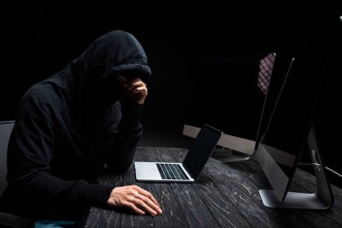 üzgün bilgisayar korsanı dizüstü bilgisayarın yanında oturuyor ve ekranı boş olan bilgisayar monitörleri siyah üzerine izole edilmiş 
