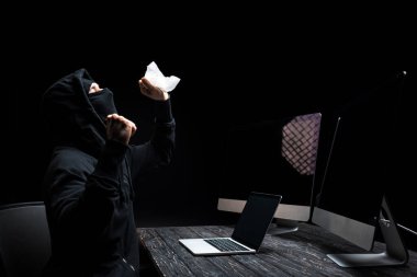 Bilgisayarın yanında dokuyu tutan duygusal hacker ve siyah ekranlı bilgisayar monitörleri. 