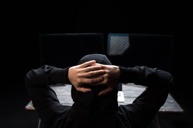 Siyah üzerine izole edilmiş boş ekranlı bilgisayar monitörlerinin yanında elleri olan kapüşonlu hacker 'ın arka görüntüsü 