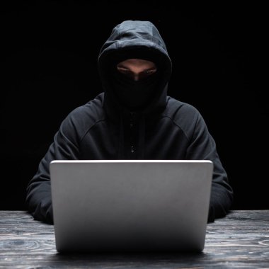 Siyah üzerine izole edilmiş dizüstü bilgisayar kullanan maskeli genç bir hacker. 