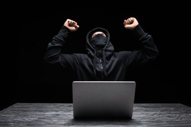Siyah dizüstü bilgisayarın yanında zaferi kutlayan maskeli heyecanlı hacker. 