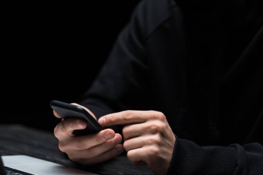 Siyah üzerine izole edilmiş akıllı telefon kullanan bilgisayar korsanı görüntüsü 