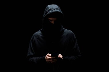 Siyah üzerinde izole akıllı telefon kullanan kapüşonlu ve maskeli bir hacker. 