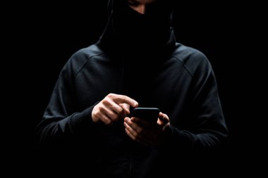 Kesilmiş bilgisayar korsanı siyah üzerine izole edilmiş akıllı telefonu işaret ediyor. 
