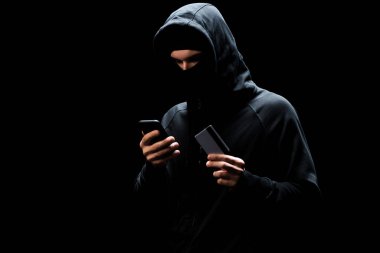 Akıllı telefon kullanan ve siyah kart kullanan maskeli bir bilgisayar korsanı. 