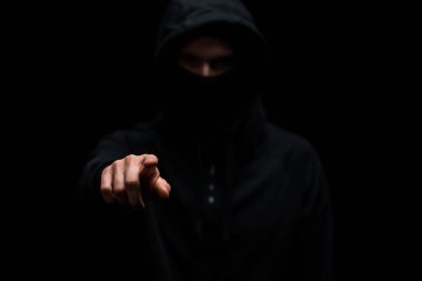 Kapüşonlu ve maskeli hacker 'ın seçici odak noktası siyah üzerine izole edilmiş parmakla işaret etmek. 
