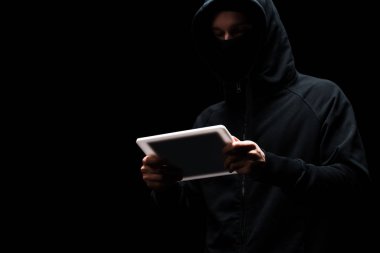 Siyah üzerine izole edilmiş dijital tablet kullanan kaputtaki isimsiz hacker 