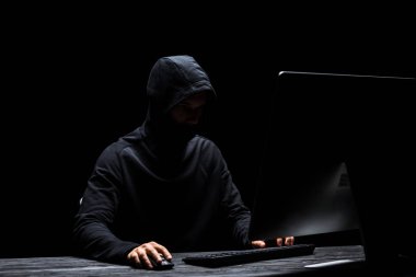 Siyah üzerine izole edilmiş bilgisayar kullanarak maskeli isimsiz bir hacker. 