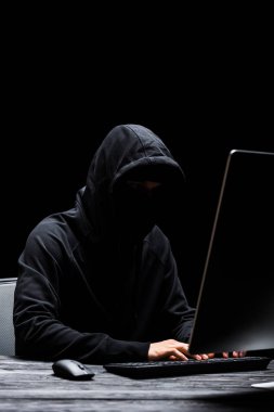 Siyah üzerine izole edilmiş bilgisayar klavyesinde maskeli isimsiz bir hacker. 