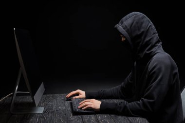 Siyah ekranlı bilgisayar monitörüne bakan kapüşonlu bilgisayar korsanı 