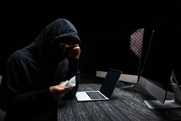 不高兴的黑客在笔记本电脑和计算机监视器附近拿着纸巾 计算机监视器上的空白屏幕与黑色隔离 — 图库照片