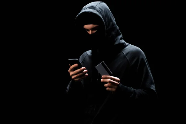 戴面具的黑客用智能手机拿着信用卡隔离在黑名单上 — 图库照片