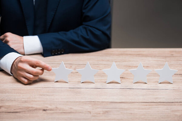 cropped view of man in formal wear pointing with finger at star isolated on grey, quality concept 