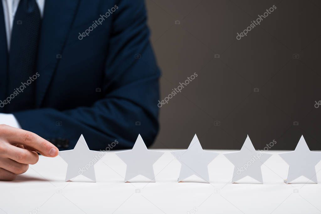 cropped view of businessman in suit touching star isolated on grey, quality concept 